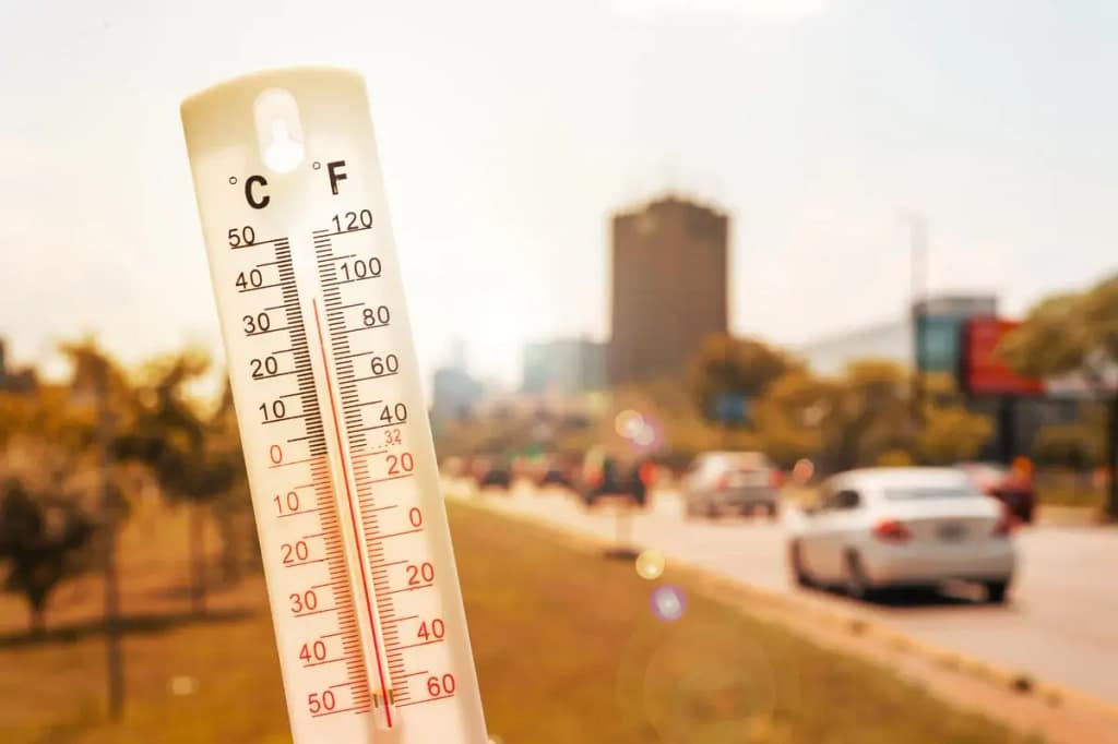 Un thermometre en premier plan avec des véhicules en second plan sous un soleil de plomb