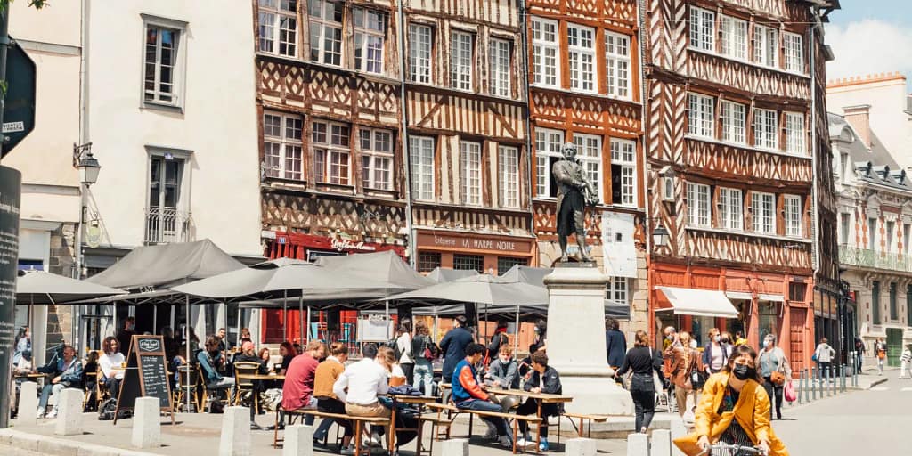 Le centre ville de Rennes avec au fond ses maisons à colombage et au premier blanc des personnes qui boivent un verre entre amis.