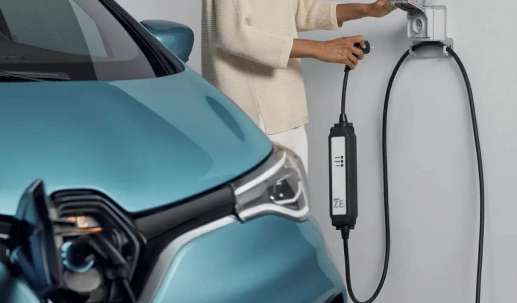 Une persone qui branche le cable d'un véhicule electrique à une prise