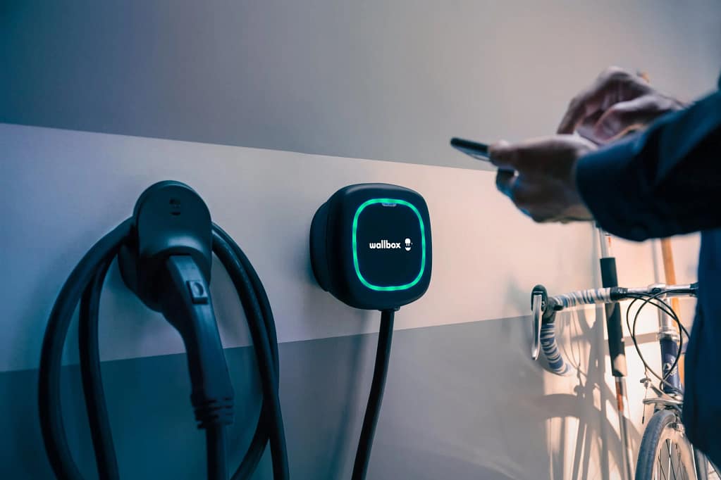 Une wallbox contre un mur avec un individu qui l'a controle depuis un smartphone