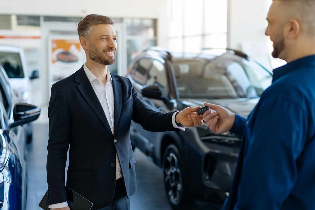 Un jeune homme recoit les clés de son véhicule électrique d'occasion remise par un commercial dans une concession automobile