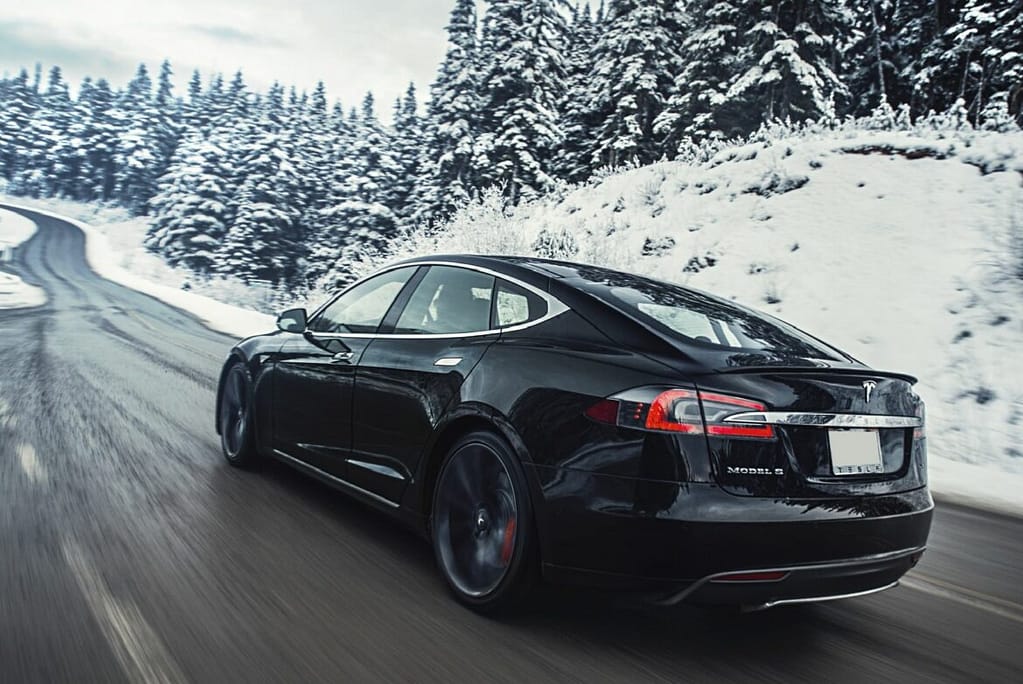 Une Tesla roule sur une route en forêt en plein hiver